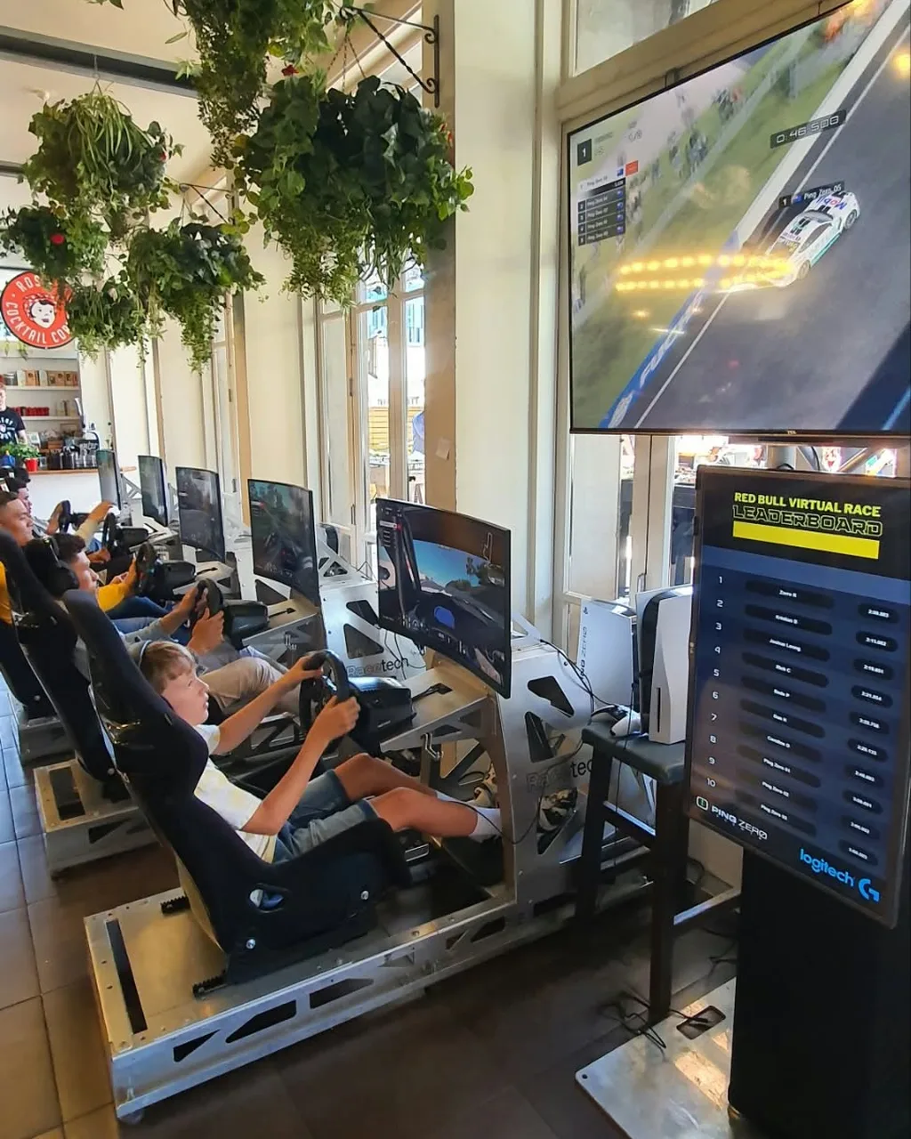 A row of Racetech sim racing rigs with drivers racing Bathurst, next to a live Red Bull Virtual Race leaderboard at an Auckland venue
